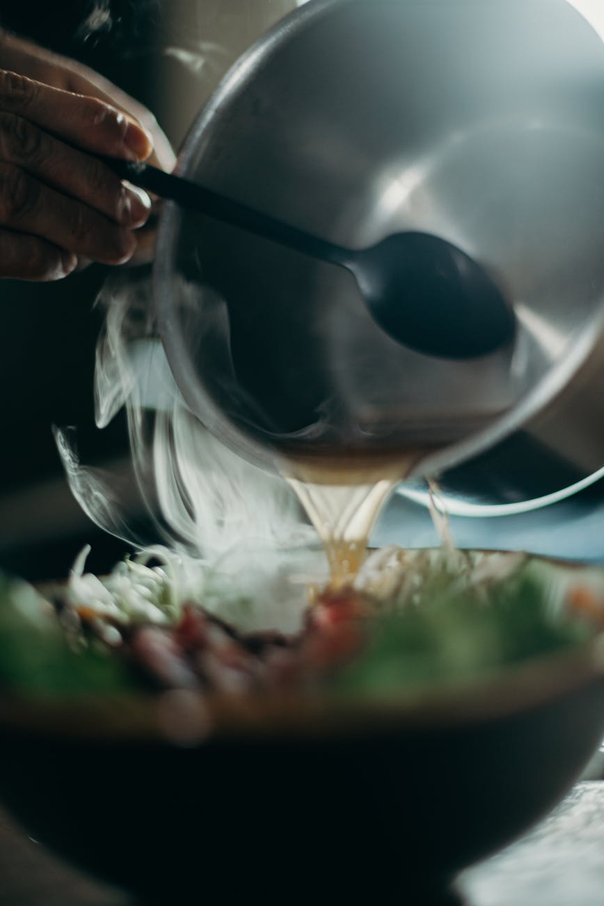 close up photo of person s hand pouring soup from stainless bowl